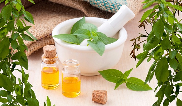 Helichrysum oil in small clear bottle, adjacent to a mortar and pestle surrounded by leaves.