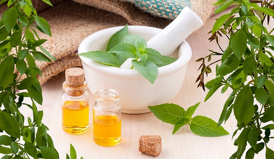 Helichrysum oil in small clear bottle, adjacent to a mortar and pestle surrounded by leaves.