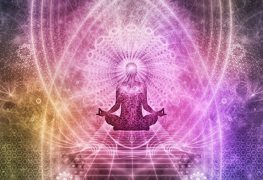 shadow figure of a person sitting and meditating with bright pink and yellow lights in the aura space surrounding him.