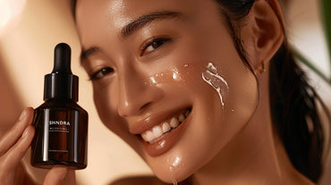 Close-up of smiling Asian woman with glowing skin holding shankara skincare oil product, demonstrating its application on her cheek.