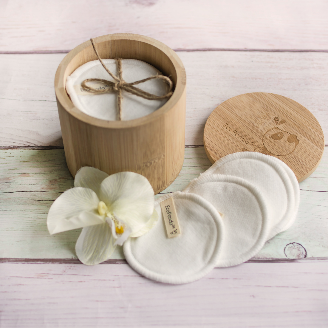 candle in wood jar on a table, flower and face pads near it.