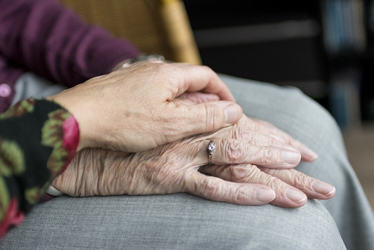 a hand placed over a pair of wrinkled hands on over the other.