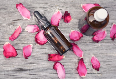 glass bottle on table with rose petals sprinkled around it.