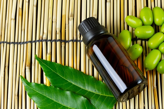 bottle of oil next to neem leaves on a wooden mat.